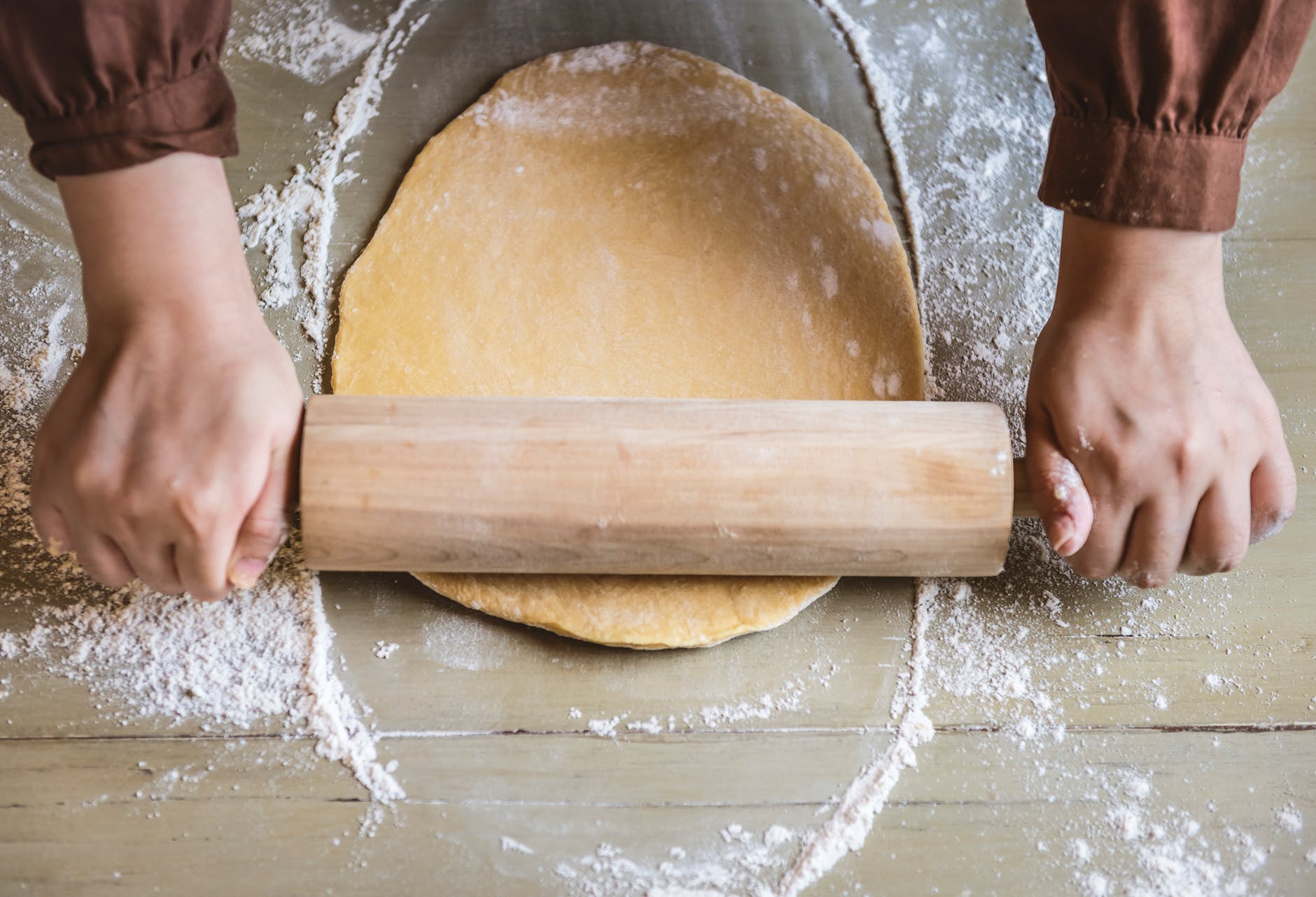 person flattening dough with rolling pin