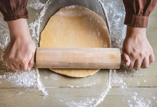 person flattening dough with rolling pin